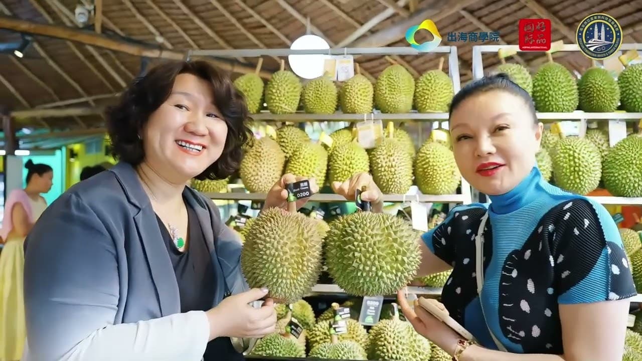 Two women smile beside a stall stacked with durians